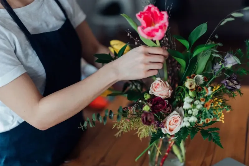 Một bình hoa tròn cổ điển với hoa hồng, hoa cúc và lá xanh, đặt trên bàn gỗ, thể hiện sự sang trọng và đầy đặn.