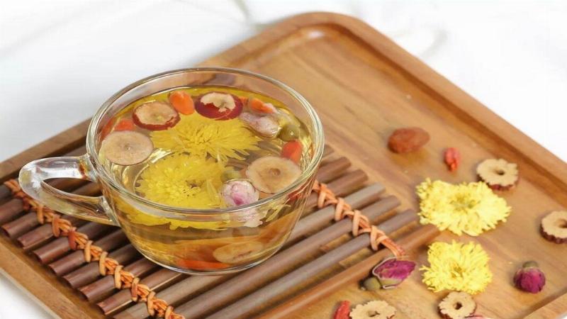 Mot ly tra hoa cuc vang nong hoi voi nhung bong hoa cuc kho noi tren be mat, canh do la mot vai bong hoa cuc tuoi va sach, minh hoa cho cong dung tot cho suc khoe cua tra hoa cuc